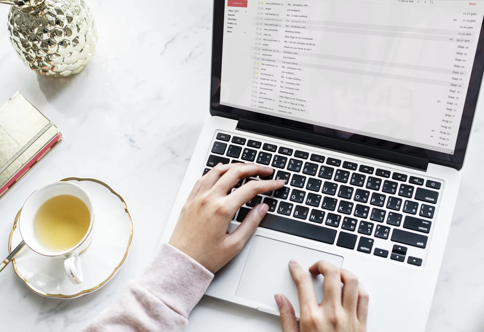 Hands typing on a laptop with the email inbox open, next to a cup of tea