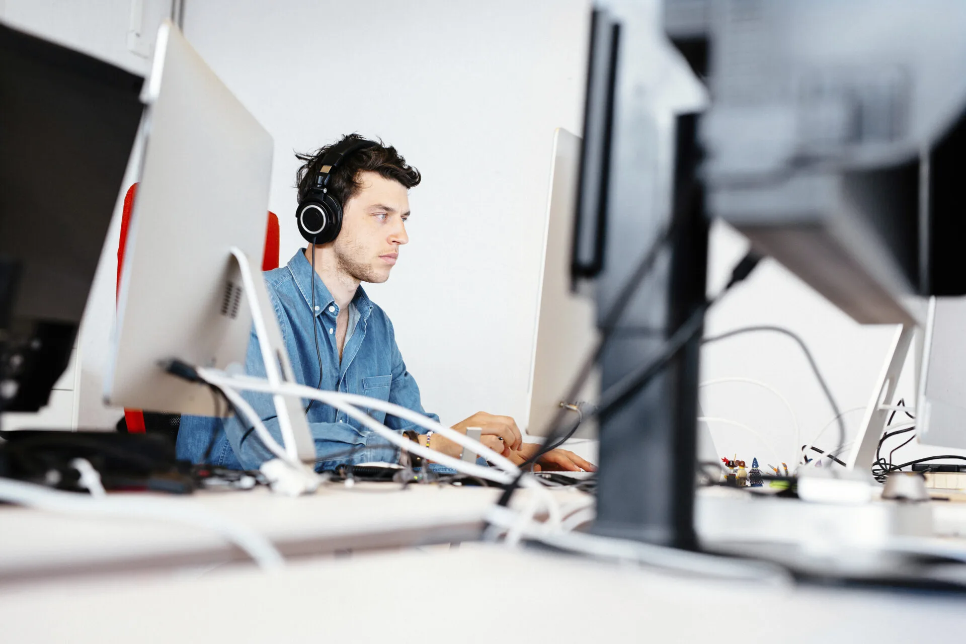 Man wearing headphones concentrating at a computer in an office with several monitors